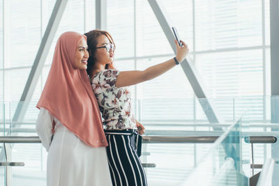 Woman taking selfie from mobile phone with friend at railroad station