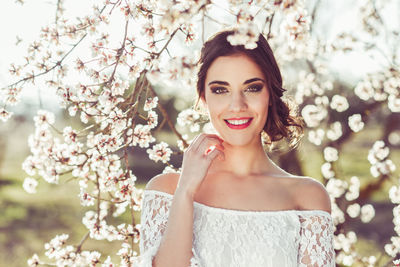 Portrait of smiling woman standing against white flowers