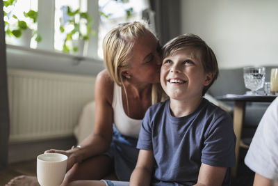 Mother kissing smiling son watching tv in living room