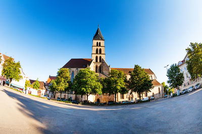 Street amidst trees and buildings against clear blue sky