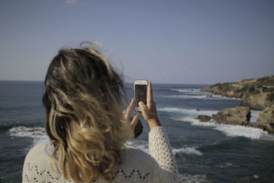 Rear view of woman photographing on beach