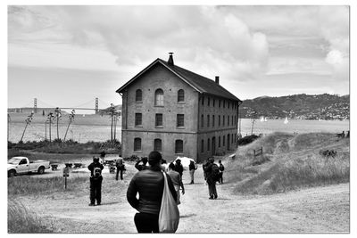 Rear view of people walking on field against buildings