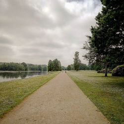 Empty footpath by road against sky