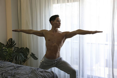 Shirtless young man doing hatha yoga at home