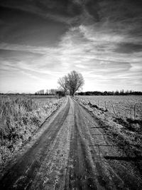 Dirt road amidst field against sky