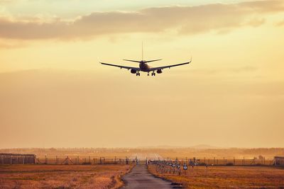 Airplane flying over road against sky during sunset