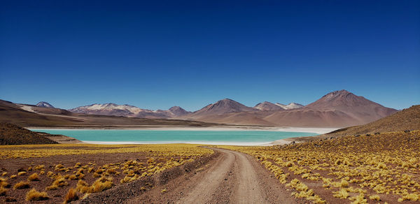 Scenic view of road by land against clear blue sky