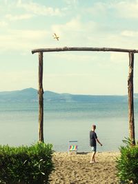 Rear view of man standing at beach against sky