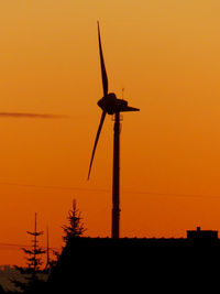 Low angle view of silhouette windmill against orange sky