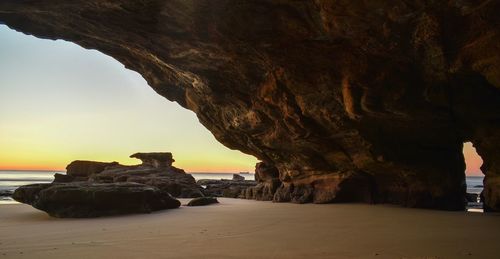 Rock formation on beach against sky during sunset