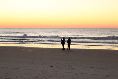 Silhouette people standing on beach against clear sky during sunset