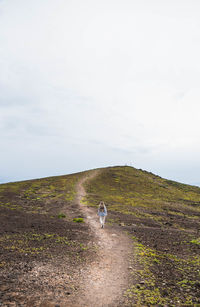 Rear view of man walking on field against sky