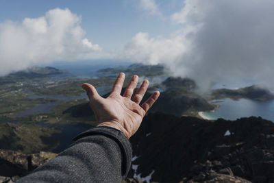 Cropped hand of person over mountains against sky