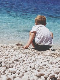 Rear view of boy sitting on pebbles at beach