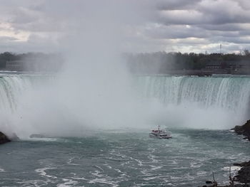 Scenic view of waterfall against cloudy sky