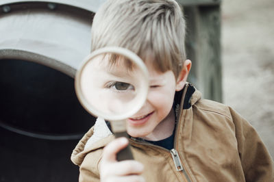 Close-up portrait of happy boy playing with magnifying glass at playground