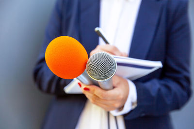 Midsection of woman holding microphone while standing against wall