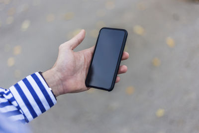 Cropped hand of person holding smart phone outdoors