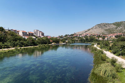 Scenic view of lake by buildings against clear blue sky