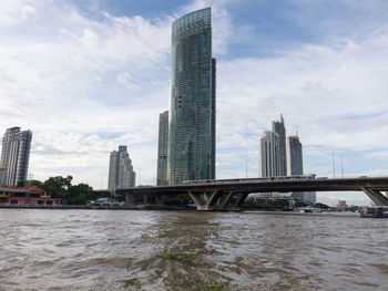 Bridge over river by buildings against sky