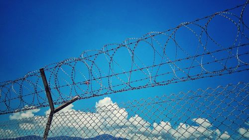 Low angle view of barbed wire fence against clear blue sky