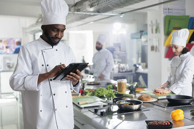 Smiling chef using digital tablet standing by kitchen counter at restaurant