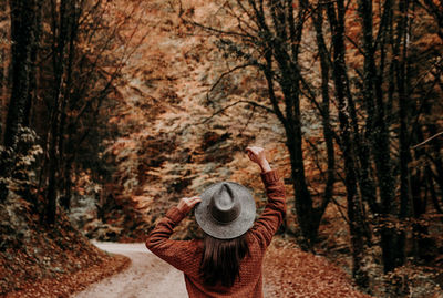 Rear view of person standing by trees in forest during winter