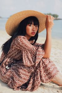 Portrait of young woman wearing hat sitting at beach