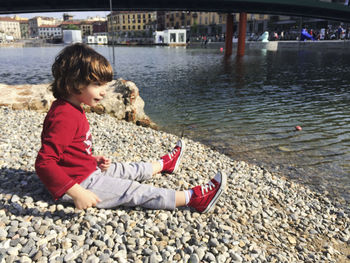 Cute boy sitting at lakeshore in city