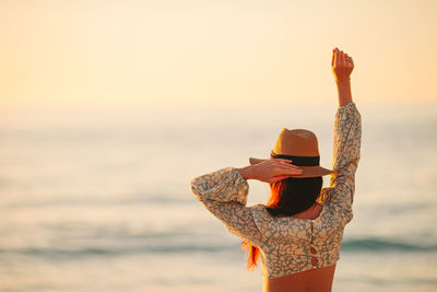 Rear view of woman standing by sea against sky during sunset