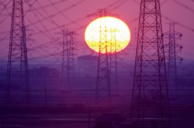 Low angle view of electricity pylon against sky during sunset