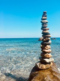 Stack of pebbles on beach against clear blue sky