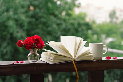 Bouquet of red rose in a vase and a book on a wooden window sill.