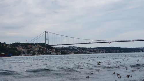 Suspension bridge over sea against cloudy sky