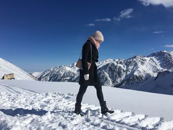 Side view of young woman walking on snowcapped mountain against blue sky