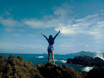 Rear view of woman standing on rock by sea against sky