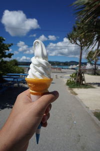 Hand holding ice cream cone against sky