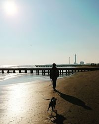 Silhouette man walking on beach against clear sky