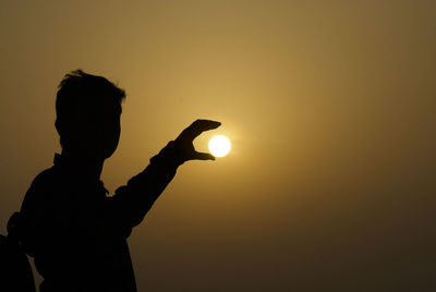 Silhouette man holding sun against sky during sunset