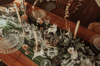 Chic christmas table setting in beige color, glassware with gold cutlery, candles, cotton, garland