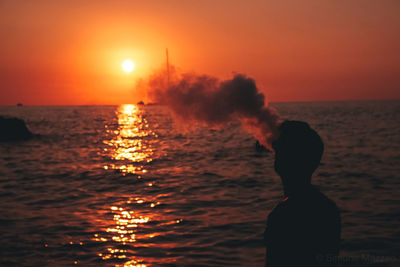 Silhouette man vaping on sea against orange sky 