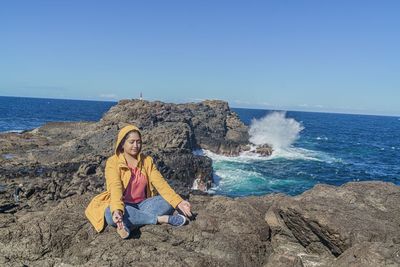 Woman sitting on rock by sea against sky