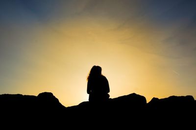 Silhouette woman sitting against sky during sunset