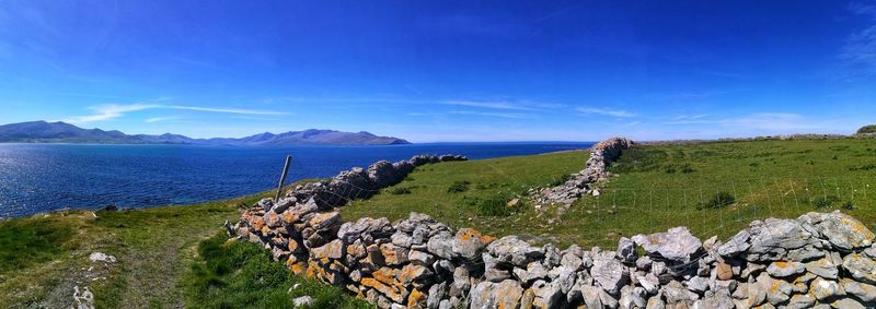 Scenic view of sea against blue sky with stone wall. county kerry. ireland.