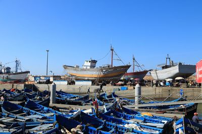 Fishing boats moored at harbor against clear blue sky