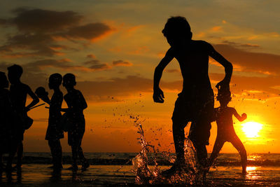 Silhouette children playing on beach against cloudy sky at sunset