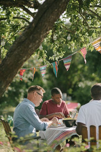 Boy eating lunch with father and grandfather at patio during garden party