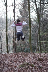 Full length of man holding umbrella on tree trunk in forest