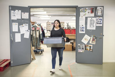 Woman carrying crate while walking out from doorway of workshop