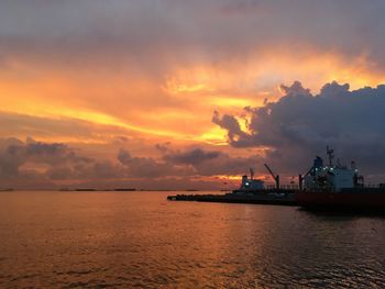 Silhouette boats in sea against dramatic sky during sunset